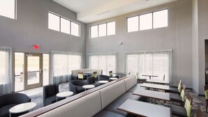 Un vaste espace intérieur aménagé avec différents coins salon, comprenant des canapés et des tables, et de grandes fenêtres qui laissent entrer la lumière naturelle.
