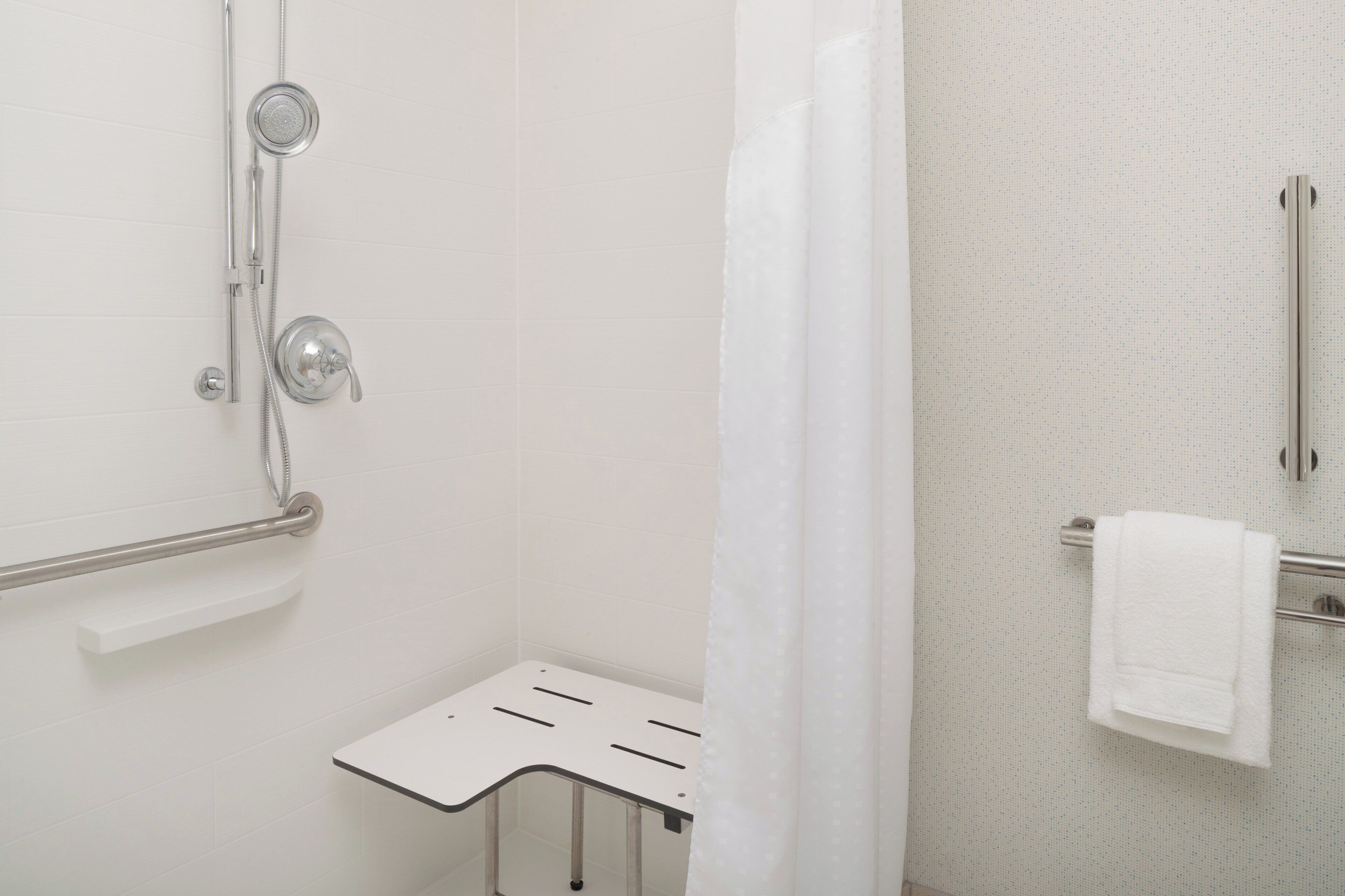A bathroom with a shower, a towel rack, and a grab bar.