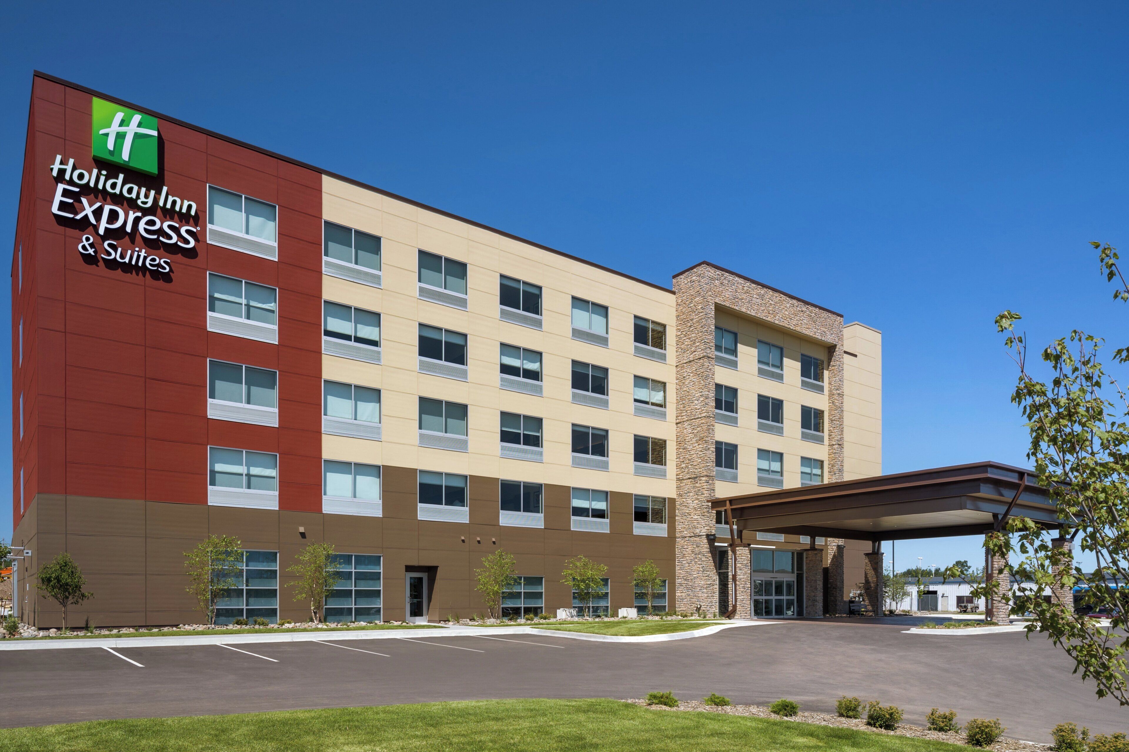 Ein Holiday Inn Express & Suites Hotel mit modernem Design, das eine Kombination aus roten und beigen Außenwänden, zahlreichen Fenstern und einem überdachten Parkbereich zeigt.
