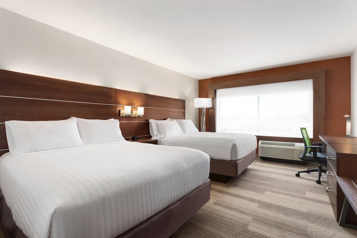 A hotel room with two beds, a desk, a chair, and a large window.
