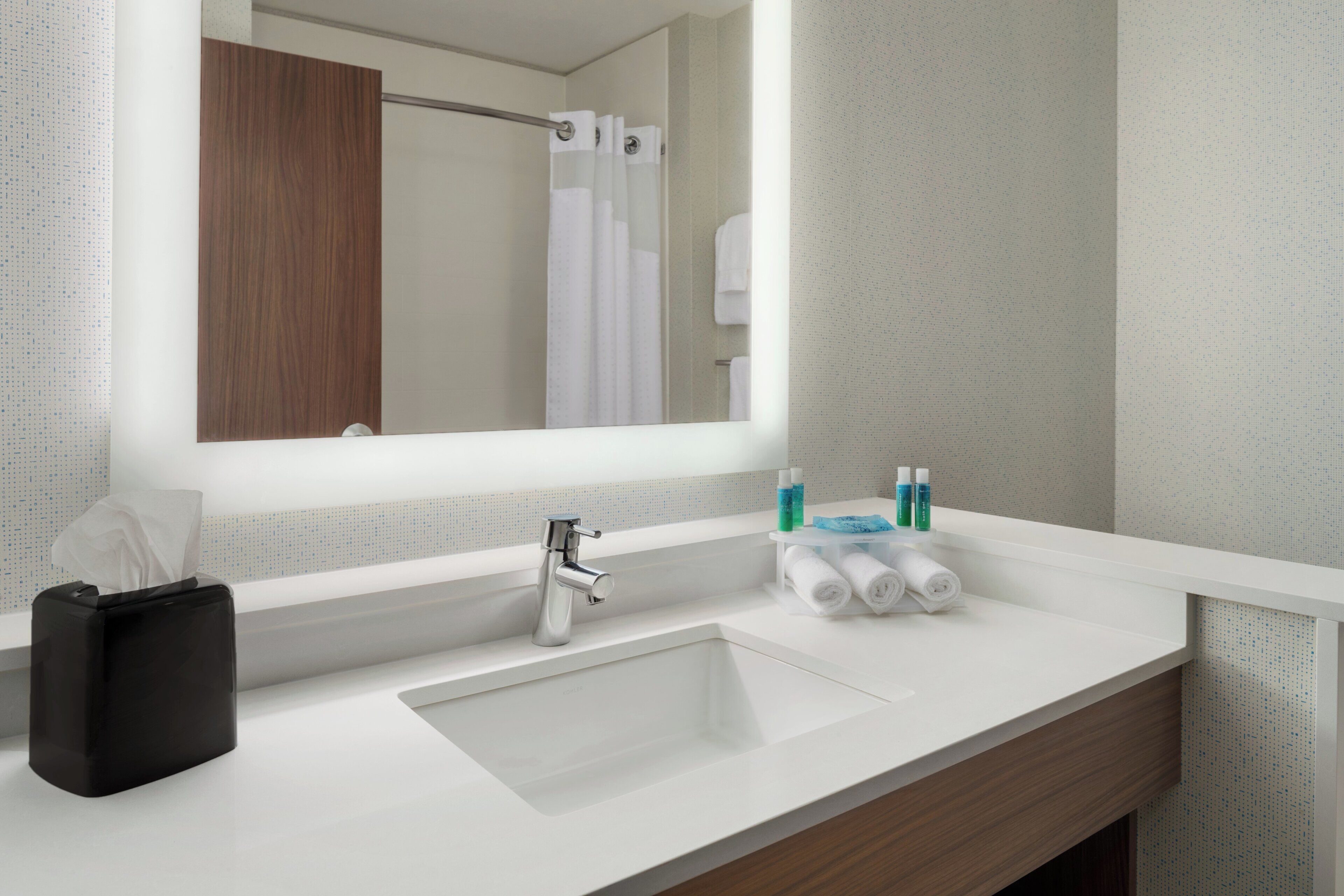 Une salle de bain moderne avec un grand miroir, un lavabo, un porte-serviettes et un sac noir.