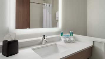 Une salle de bain moderne avec un grand miroir, un lavabo, un porte-serviettes et un sac noir.