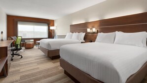Una habitación de hotel con dos camas, un escritorio, una silla y un ventanal grande.