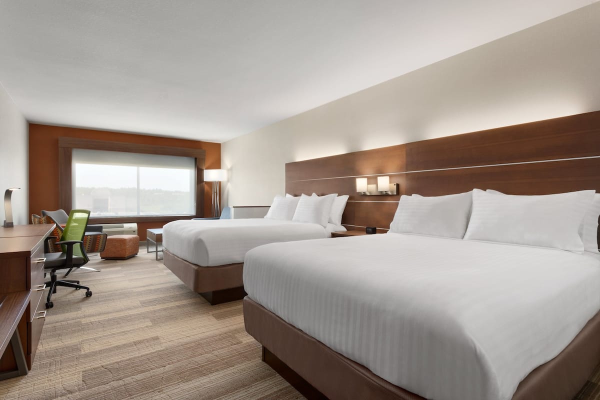 A hotel room with two beds, a desk, a chair, and a large window.