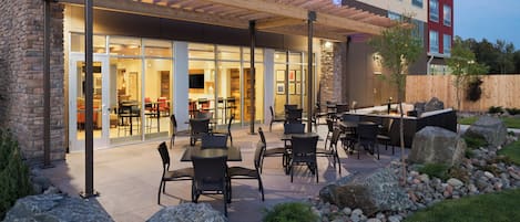 An outdoor patio area with tables and chairs, a stone wall, and a view of the building's interior.