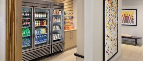 A corridor with a vending machine stocked with beverages, a refrigerator, and a wall-mounted artwork.