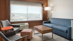 A modern hotel room with a large window, a blue sofa, a grey armchair, a wooden coffee table, and a small orange table. - Holiday Inn Express & Suites Duluth North - Miller Hill by IHG (Duluth)