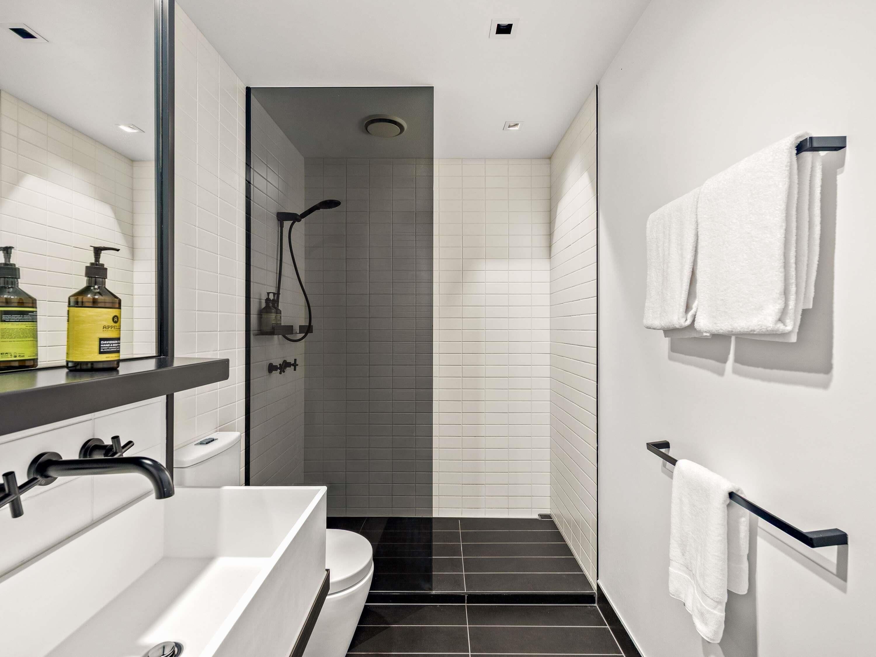 Un baño moderno con lavamanos blanco, grifo negro y zona de ducha.