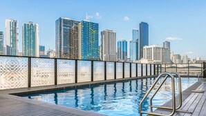 A rooftop pool with a city skyline view, metal railings, and a wooden deck. - Peppers Southern Cross Melbourne (Docklands)