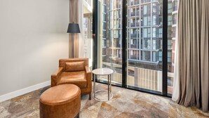 A modern room with a leather armchair, a small round table, and a large window with curtains. - Peppers Southern Cross Melbourne (Docklands)