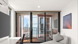 A modern bedroom with a bed, a desk, a chair, and a view of a cityscape through large glass doors. - Peppers Southern Cross Melbourne (Docklands)
