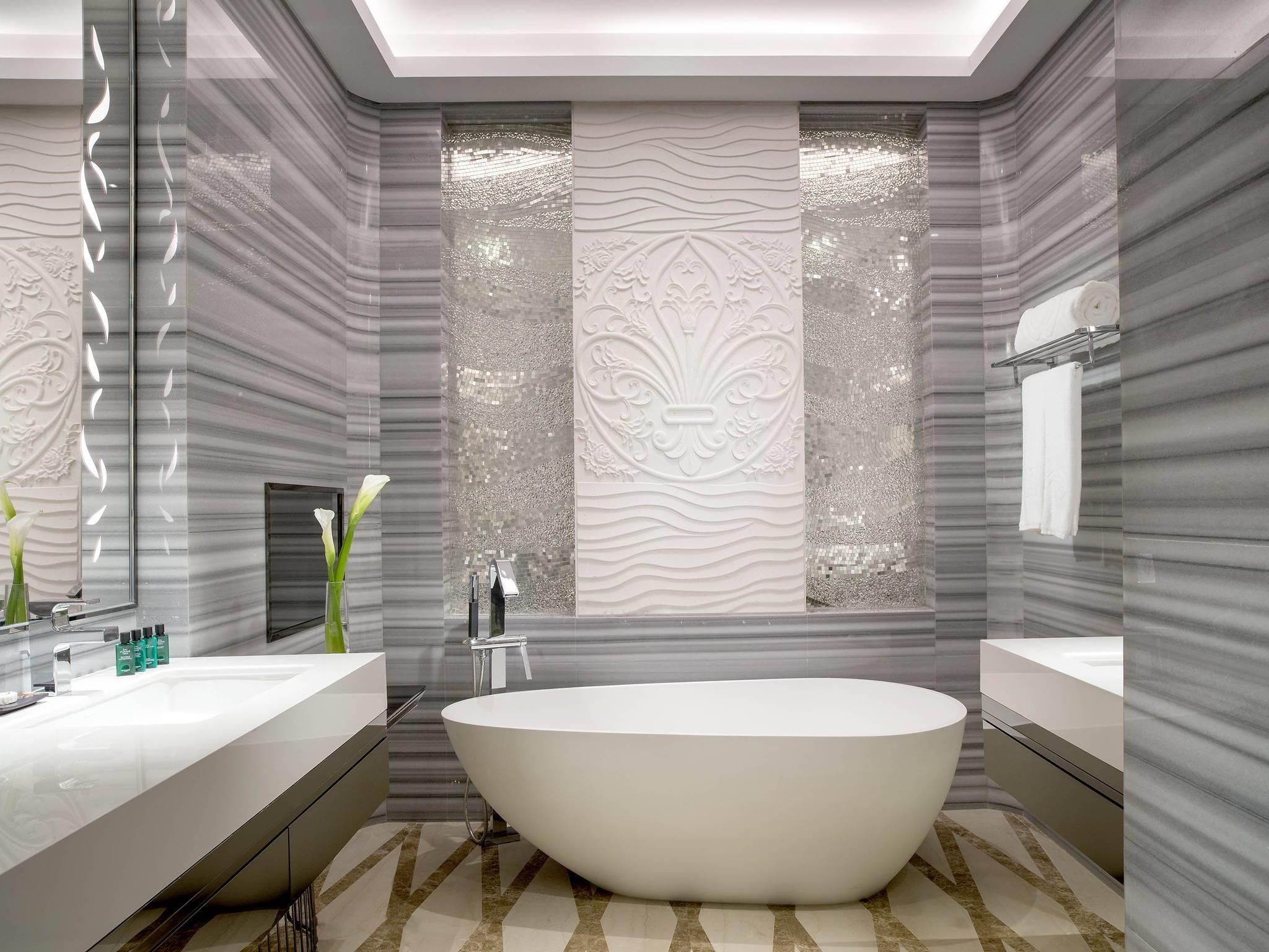 A modern bathroom with a freestanding bathtub, two vanity mirrors, and decorative wall panels.