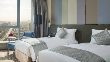 Habitación de hotel con dos camas, vista a la ciudad, una lámpara y una mesita con un jarrón de flores.