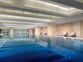 Una piscina interior moderna con agua cristalina, sillas de descanso e iluminación empotrada.