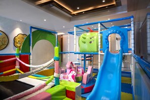 Un espace de jeux pour enfants avec un toboggan, des structures de jeux en mousse et une zone d’escalade avec des filets.