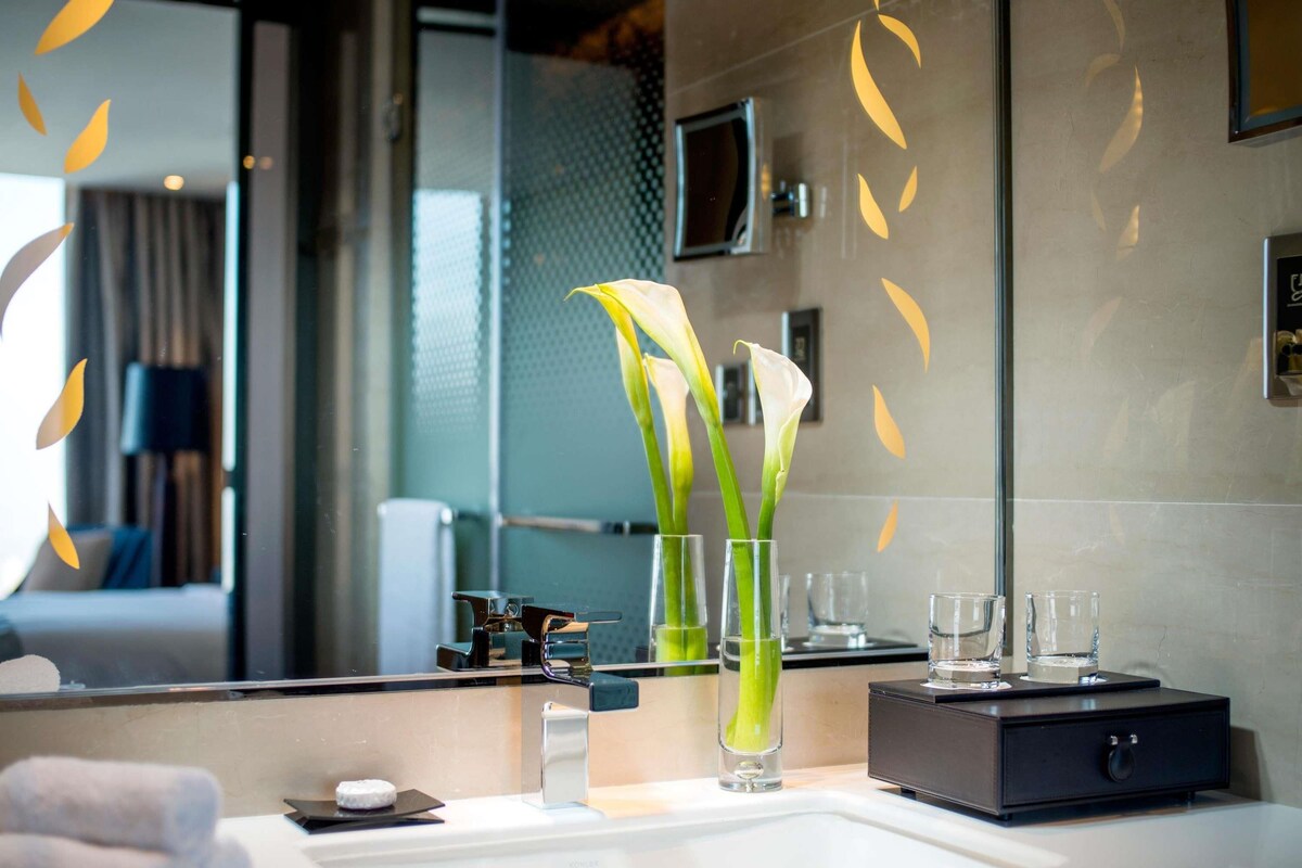 A modern bathroom with a large mirror, a sink, and two vases with white flowers.