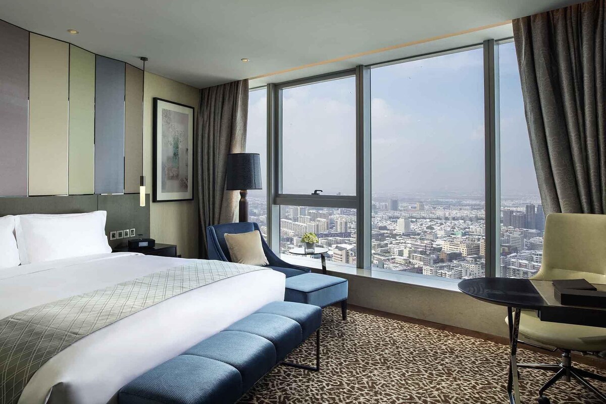 Une chambre d’hôtel avec un grand lit, un bureau, une chaise et une vue sur le paysage urbain.