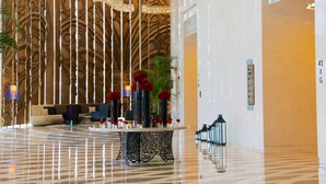 Eine Lobby mit einem gemusterten Wanddesign, einem Empfangstresen mit Rosenvasen und einer Sitzecke mit Sofas und Sesseln.
