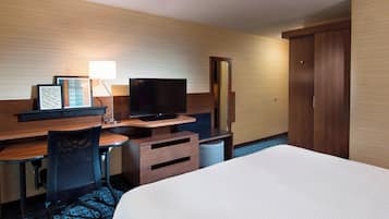 Habitación de hotel con una cama, un escritorio con televisor, una silla, una lámpara de escritorio y un armario.