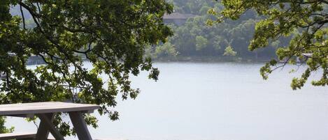 A lakeside picnic table with a view of a calm lake and surrounding trees.