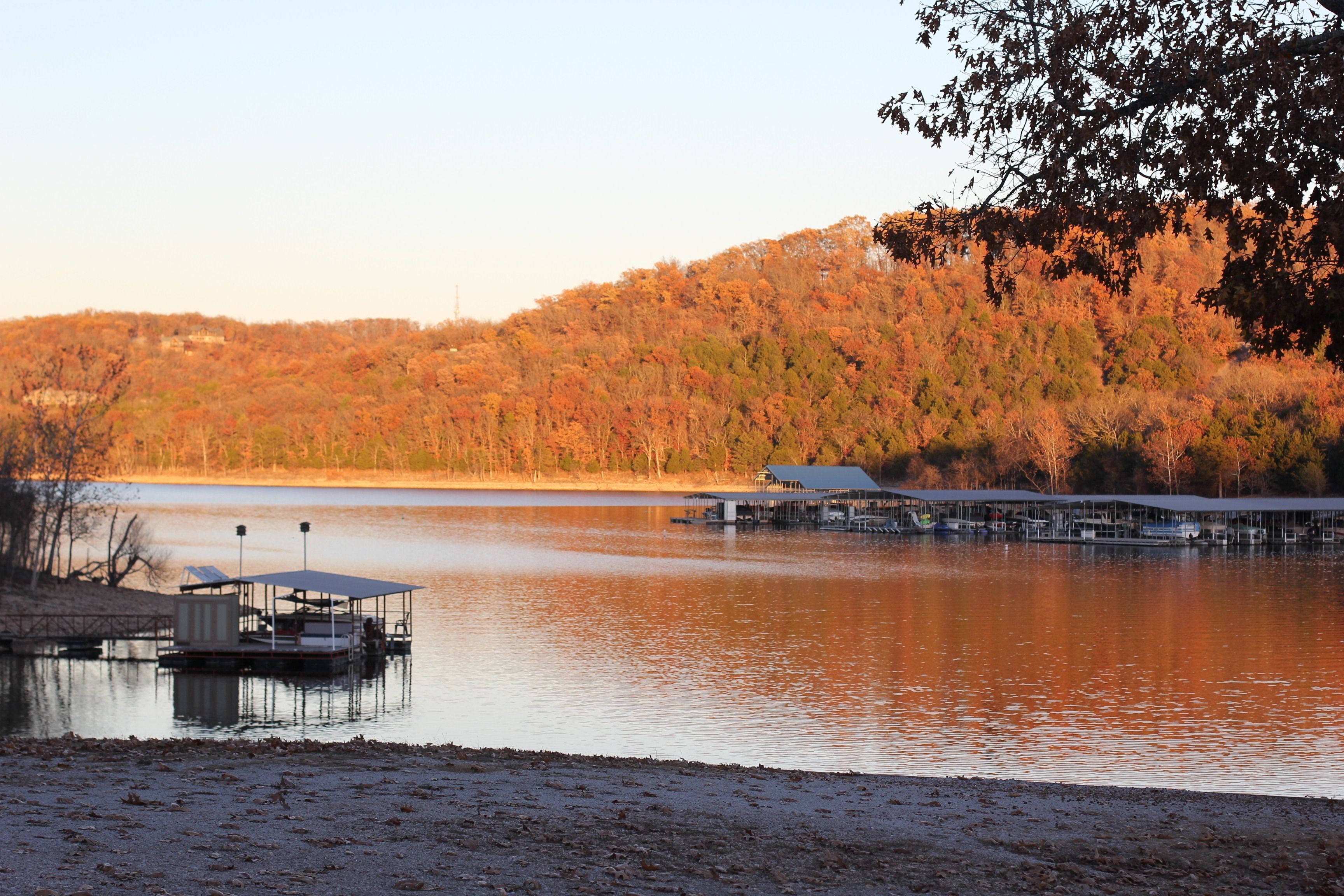 A lakeside dock with a covered structure and a forested hillside in the background.