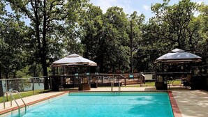 Una piscina con un área de terraza amurallada, rodeada de árboles y con sombrillas.