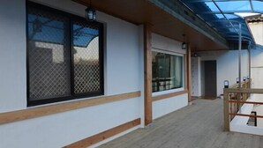 Un pasillo con suelo de madera, un espacio techado con techo transparente y ventanas amplias con mosquiteras.