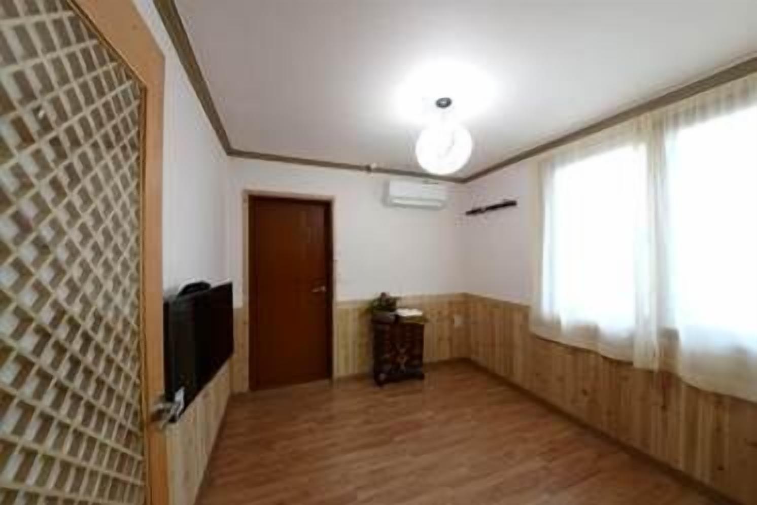 Una habitación con paneles de madera, una puerta, una mesita con una planta y un televisor en la pared izquierda.