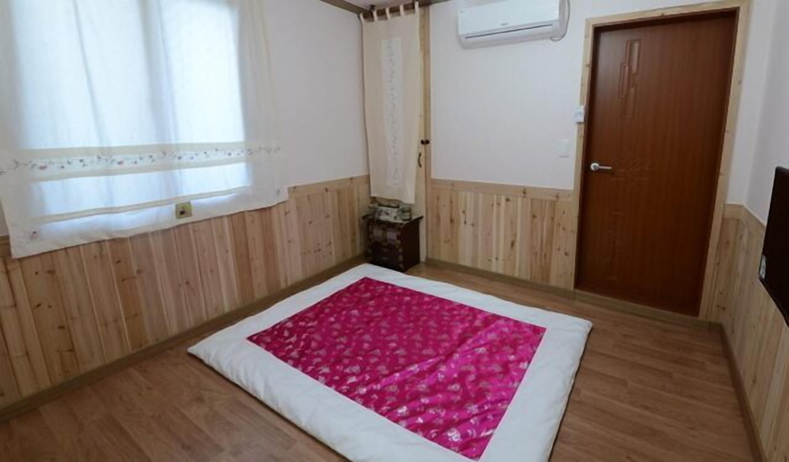 Una habitación con paneles de madera, una puerta de madera, una ventana con cortinas y una alfombra rosa estampada.