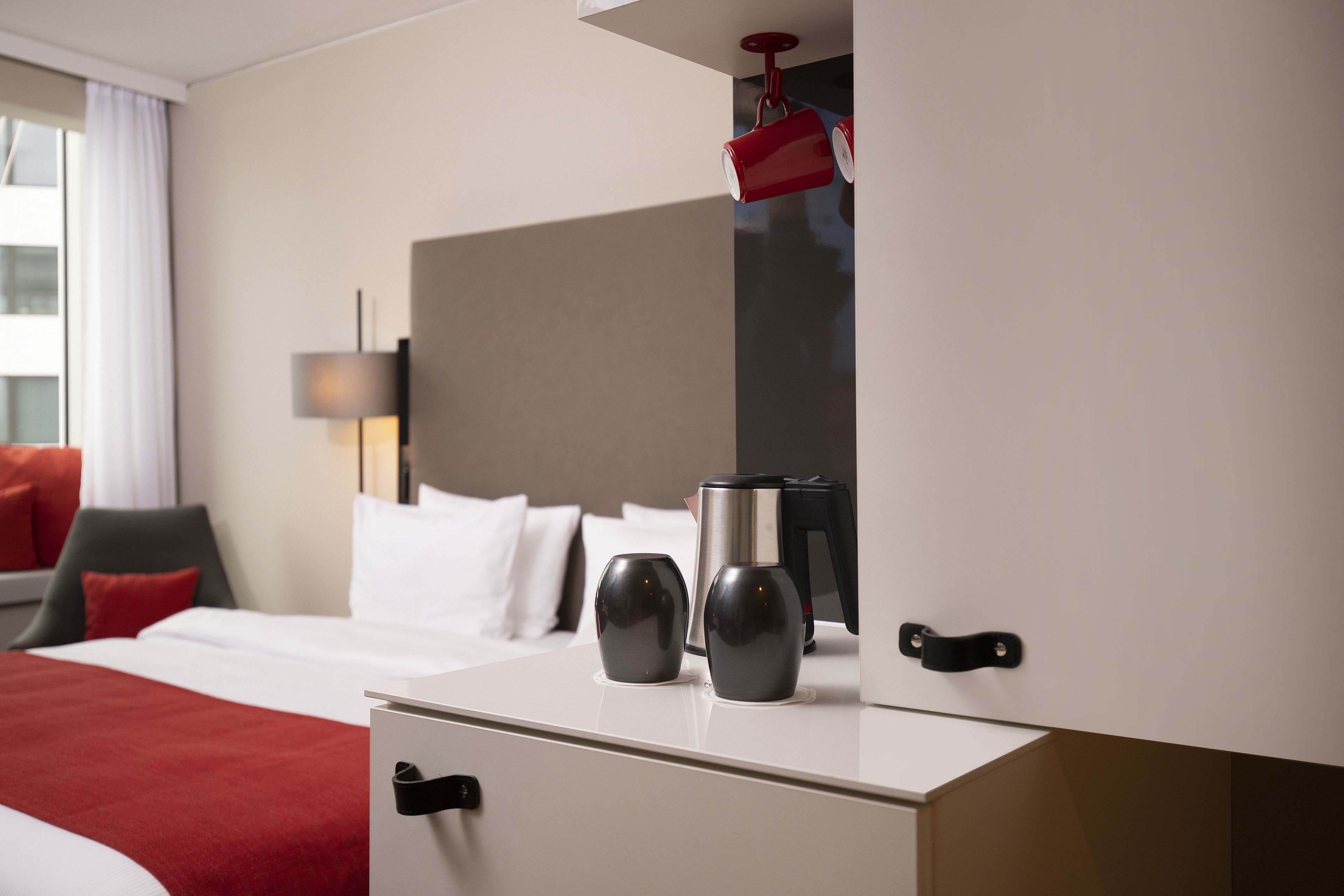 A hotel room with a bed, a desk, a coffee maker, and a red mug hanging from the ceiling.