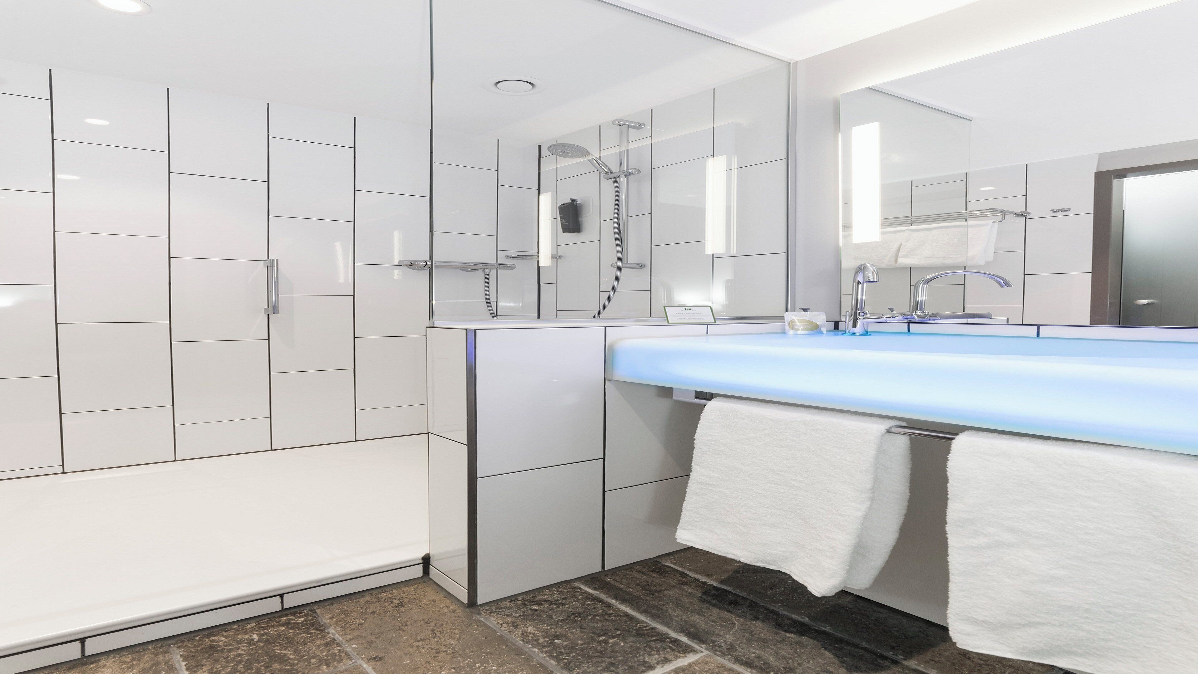 A modern bathroom with a walk-in shower, a large mirror, and a blue sink.