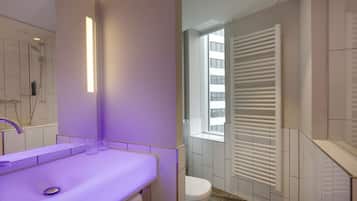 A modern bathroom with a purple-lit vanity, a shower, and a toilet with a window and blinds.