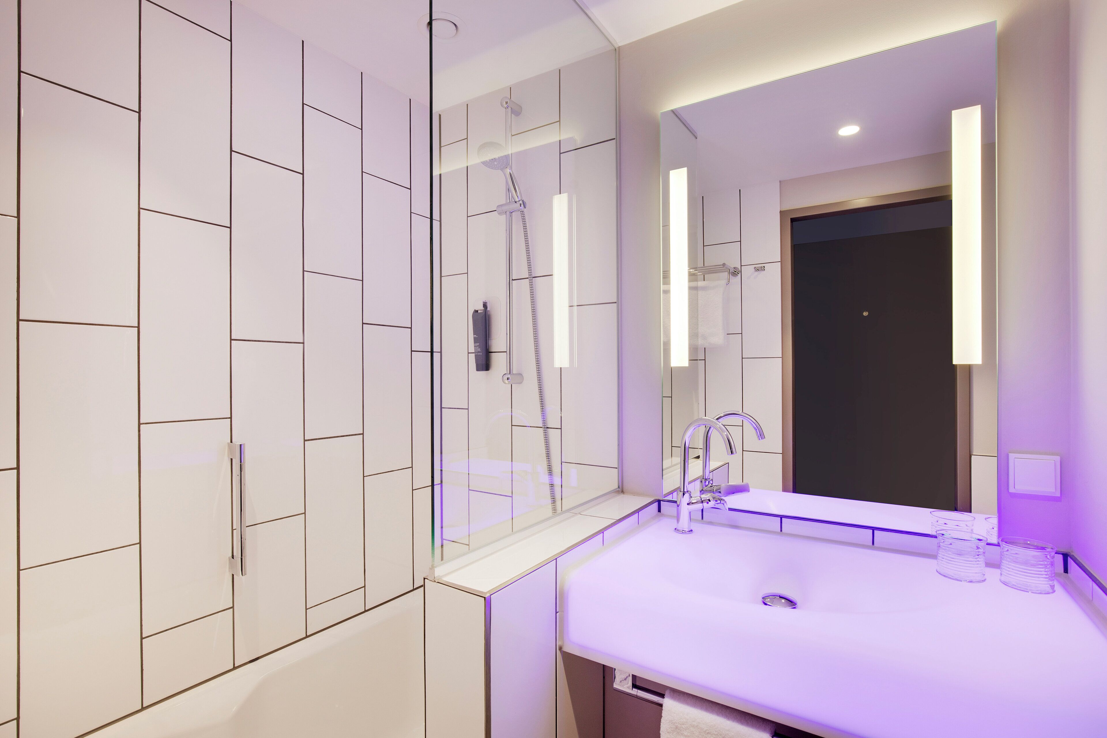 A modern bathroom with a glass-enclosed shower, a white sink with a mirror above it, and a dark door in the background.