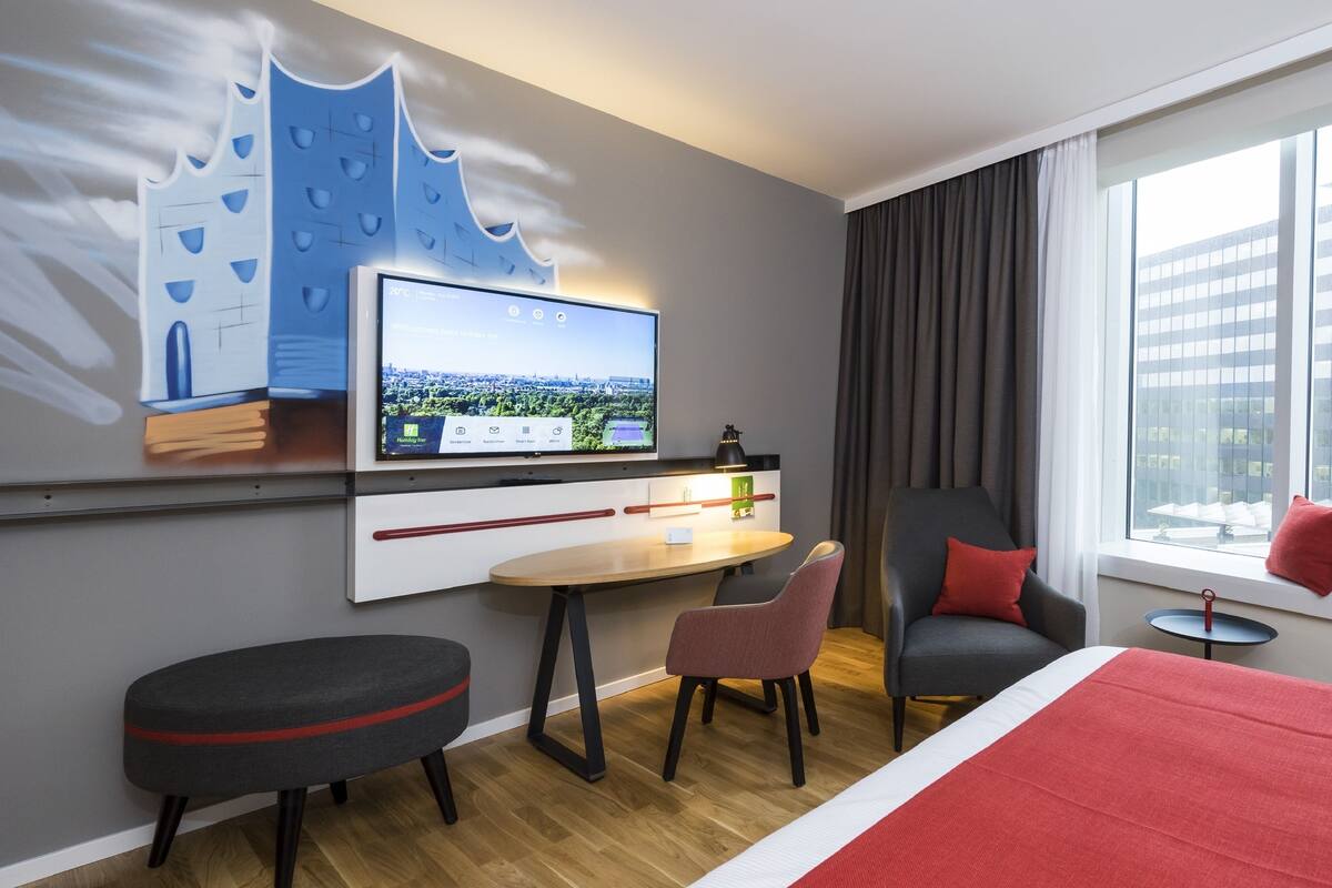 Une chambre d’hôtel moderne, dotée d’un grand lit, d’un bureau avec un ordinateur, d’une chaise et d’une fenêtre avec des rideaux.