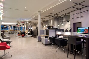 Een moderne werkplek met hoge tafels, stoelen en een groot beeldscherm.