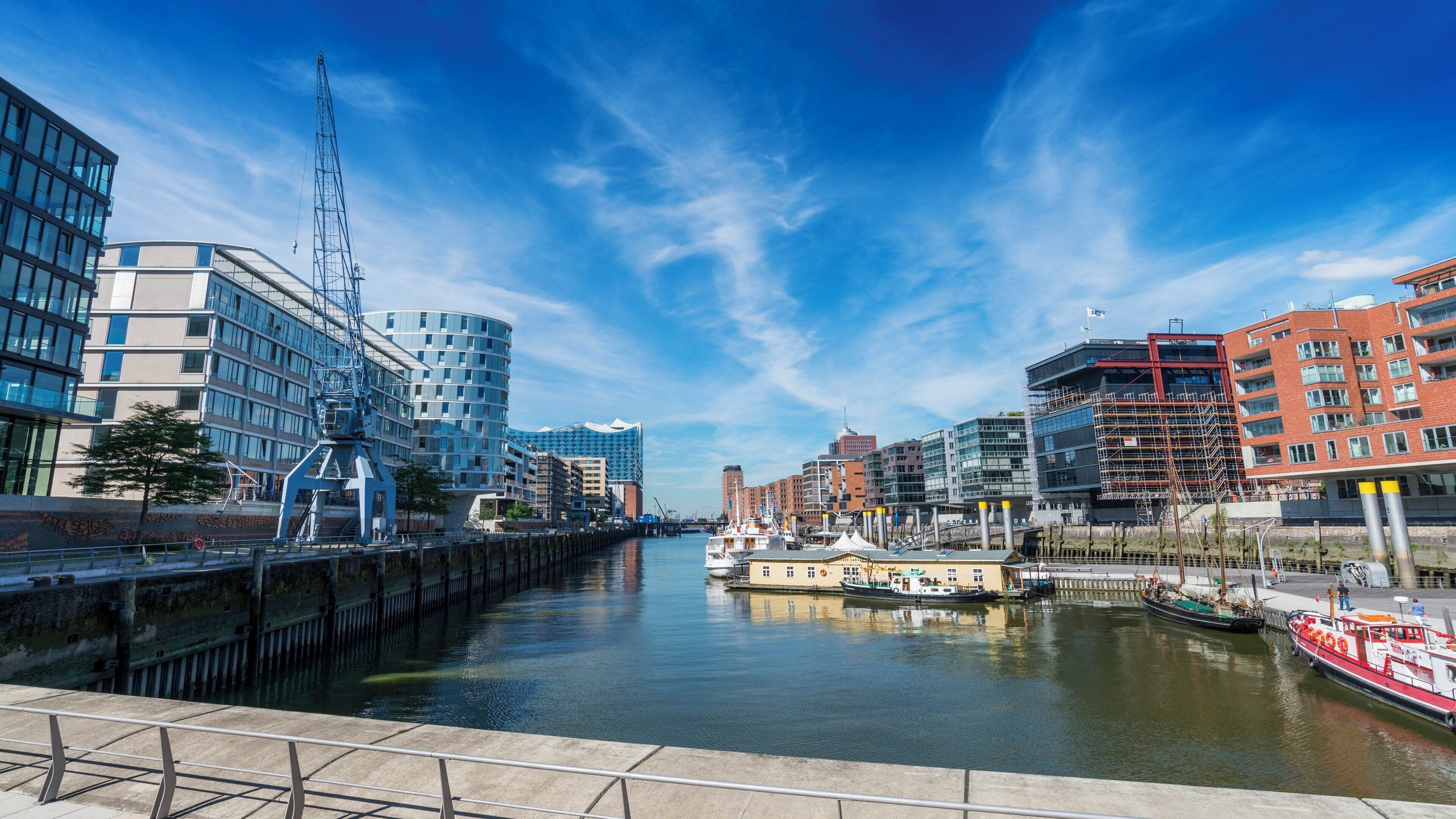 A waterfront cityscape with modern buildings, a marina, and a clear sky.