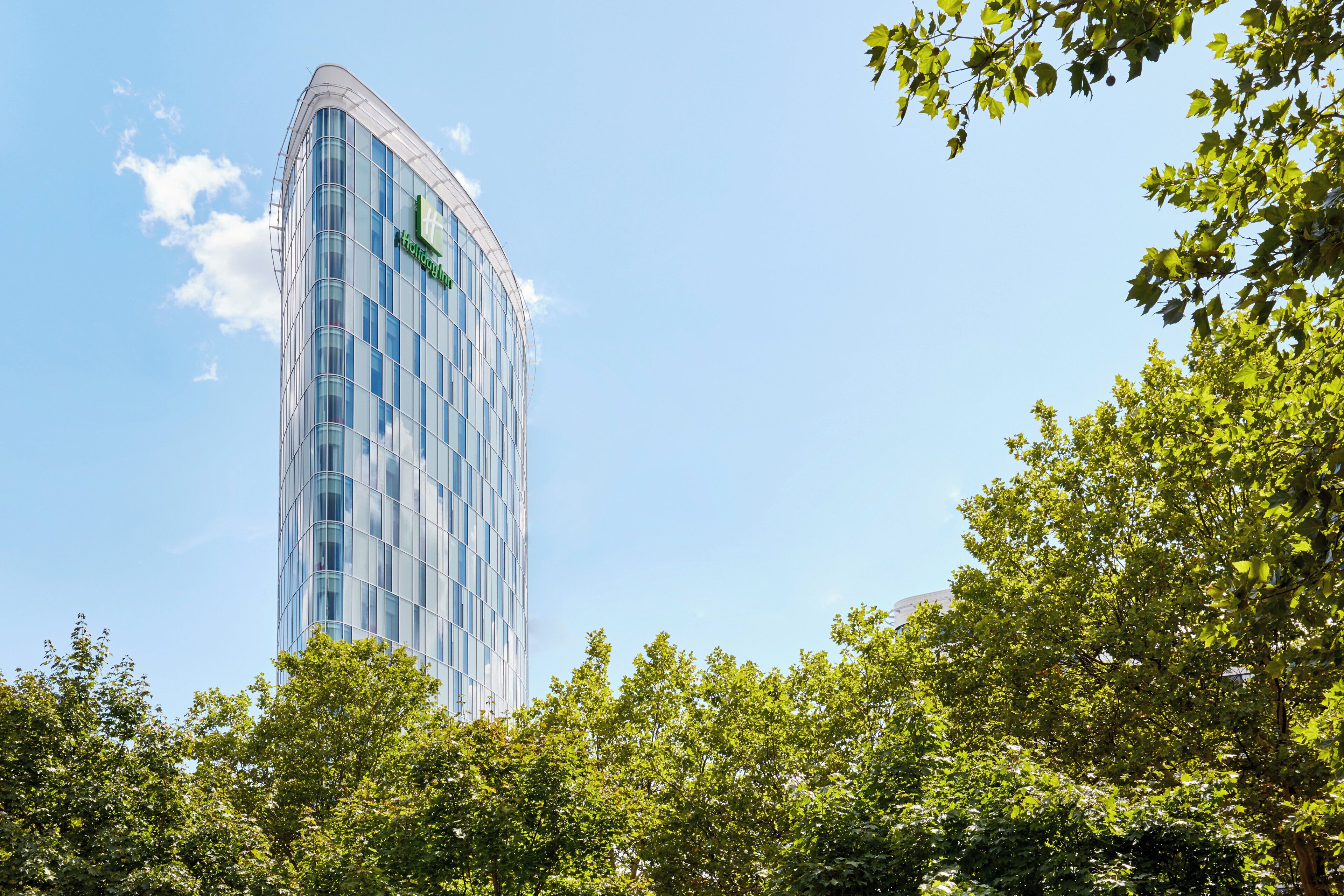 Un immeuble moderne de grande hauteur, doté d’une façade incurvée en verre, entouré d’arbres verdoyants.