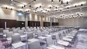 Une salle de conférence avec des rangées de chaises grises, une moquette à motifs et un plafond doté de plusieurs luminaires.