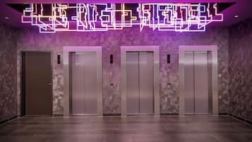 Ein moderner Aufzugsbereich mit vier Aufzügen und einer geometrischen Lichtinstallation an der Decke.