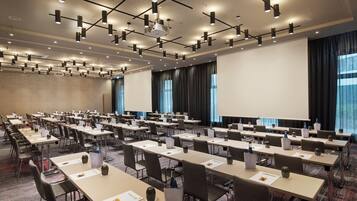 A conference room with multiple tables and chairs, a large screen, and a ceiling with recessed lighting.