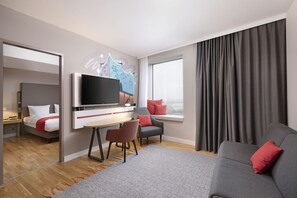 Ein modernes Hotelzimmer mit Flachbildfernseher, einer Couch, einem Sessel, einem Schreibtisch und einem Bett.