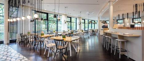 A spacious indoor dining area with multiple tables and chairs, large windows, and hanging pendant lights.