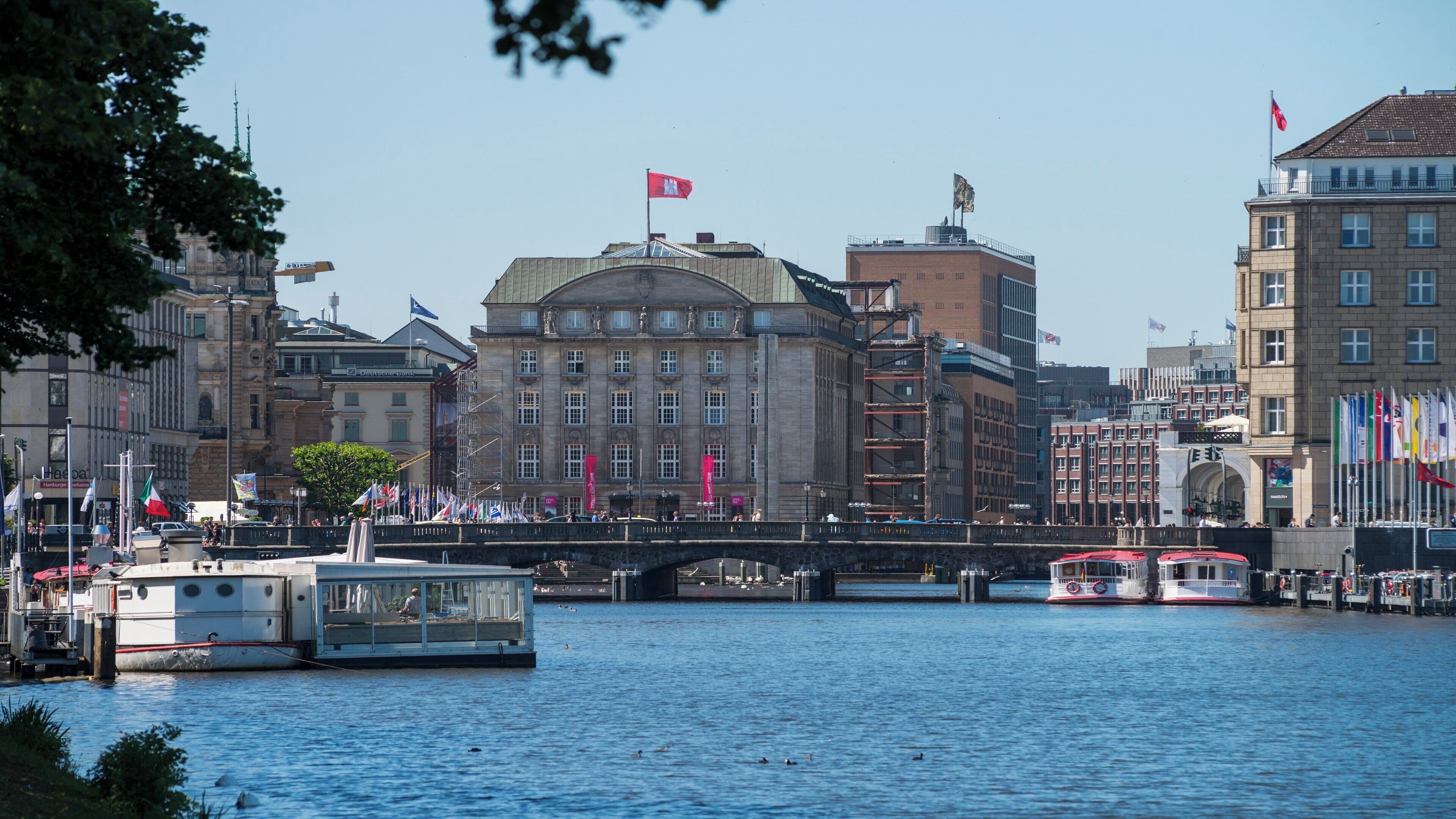 A river with boats, a bridge, and buildings with flags.