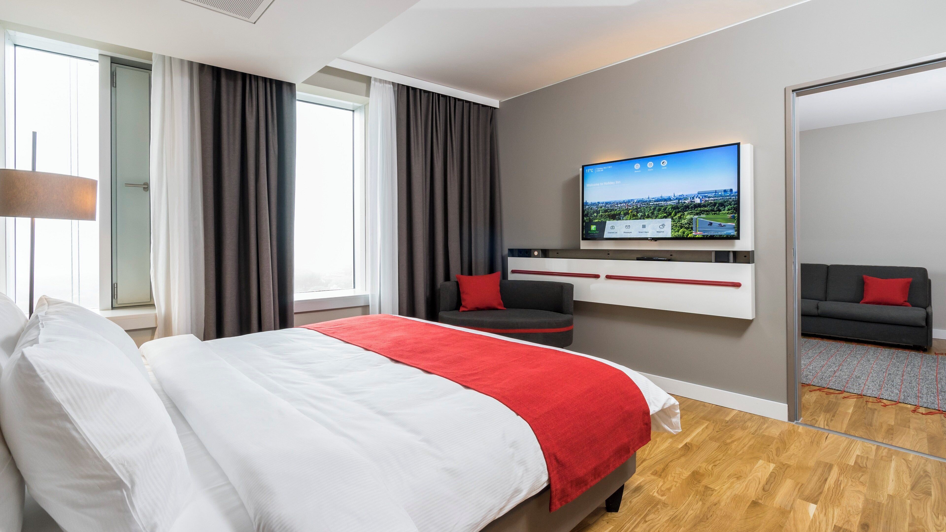 Ein modernes Hotelzimmer mit einem großen Bett, einem flachbildfernseher an der Wand, einer Couch und einem Schreibtisch.