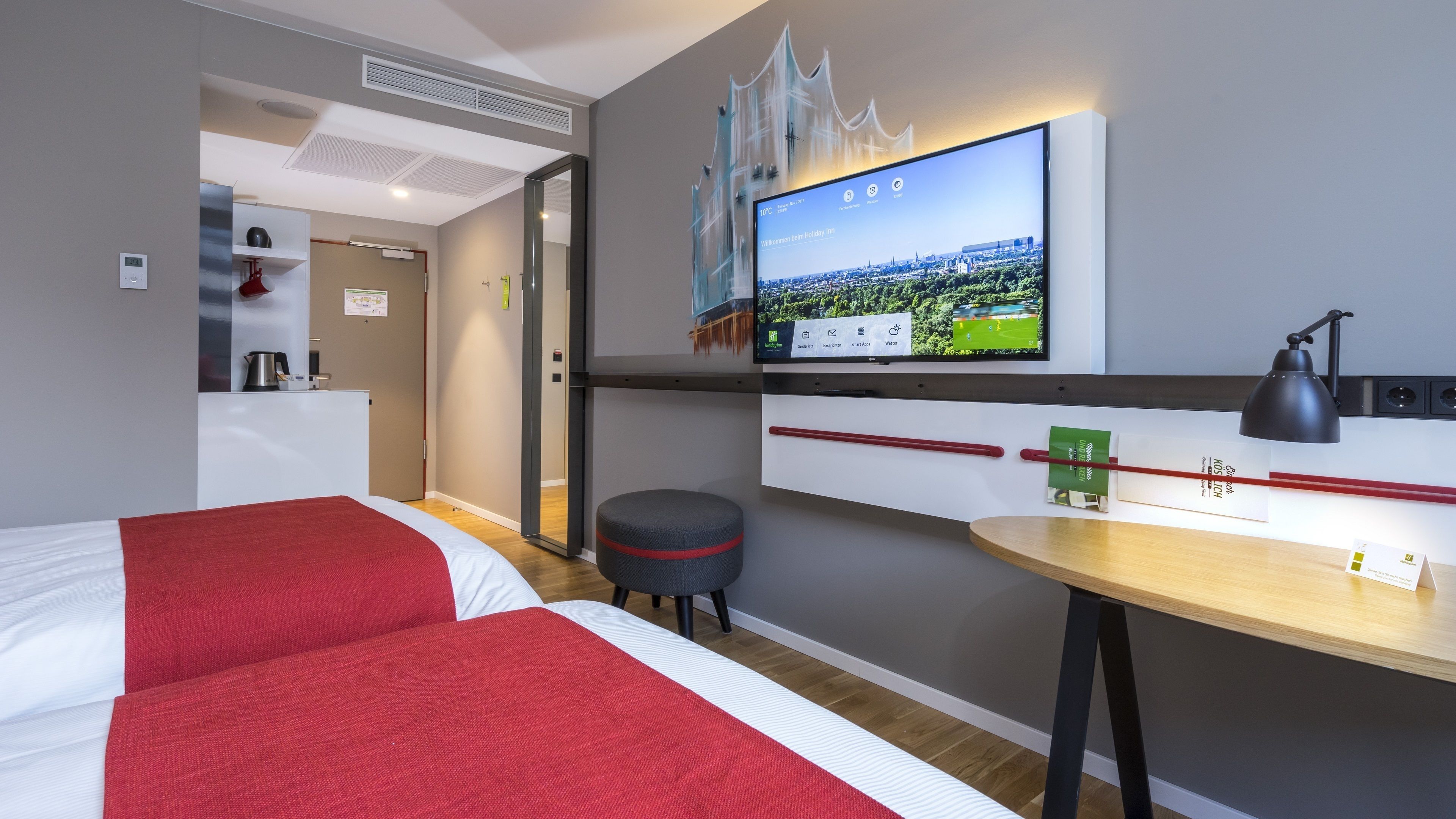 Een hotelkamer met twee bedden, een bureau, een televisie en een klein krukje.