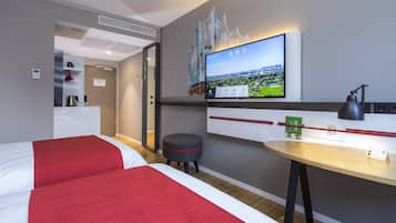 A hotel room with two beds, a desk, a television, and a small stool.