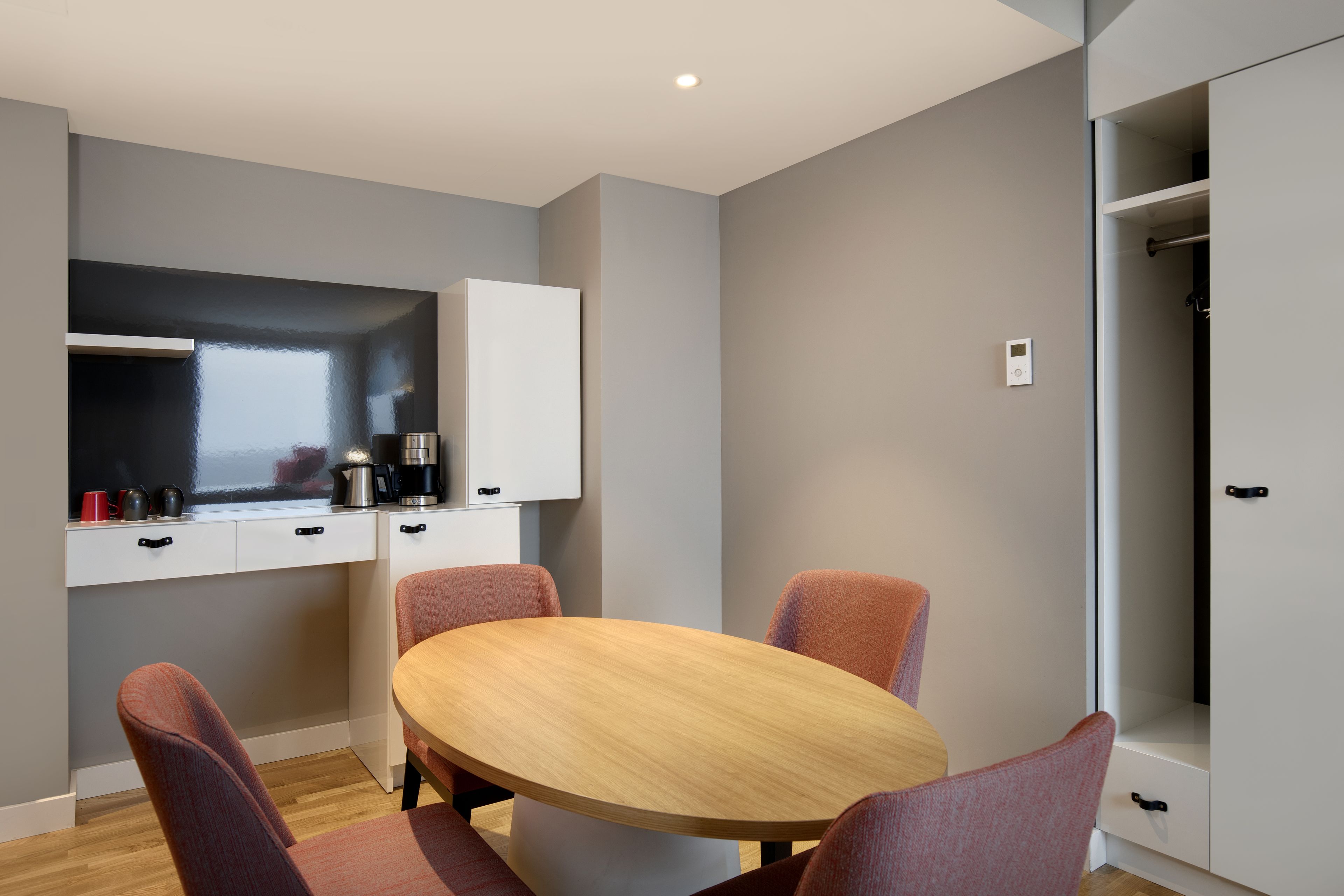 A modern kitchen with a round wooden table and four chairs, a white cabinet, and a built-in oven.