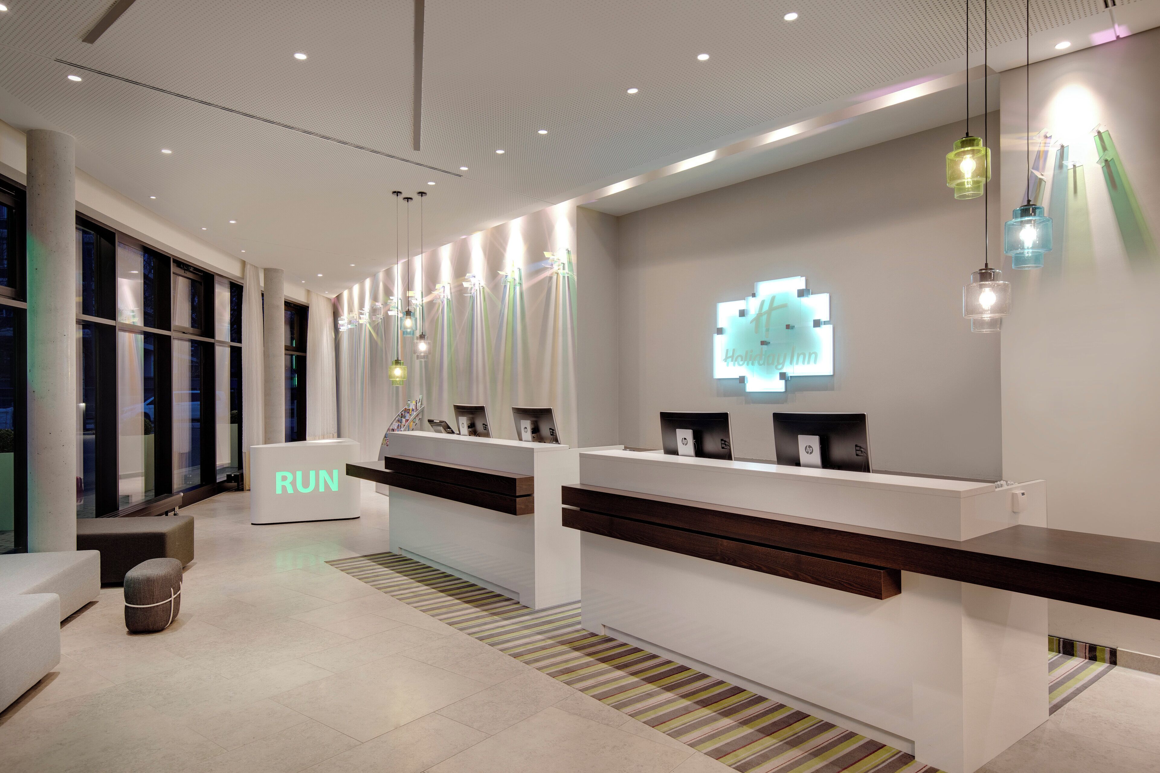 A modern hotel reception area with a white reception desk, a 'RUN' sign, and a logo on the wall.