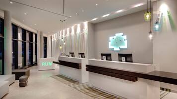 A modern hotel reception area with a white reception desk, a 'RUN' sign, and a logo on the wall.