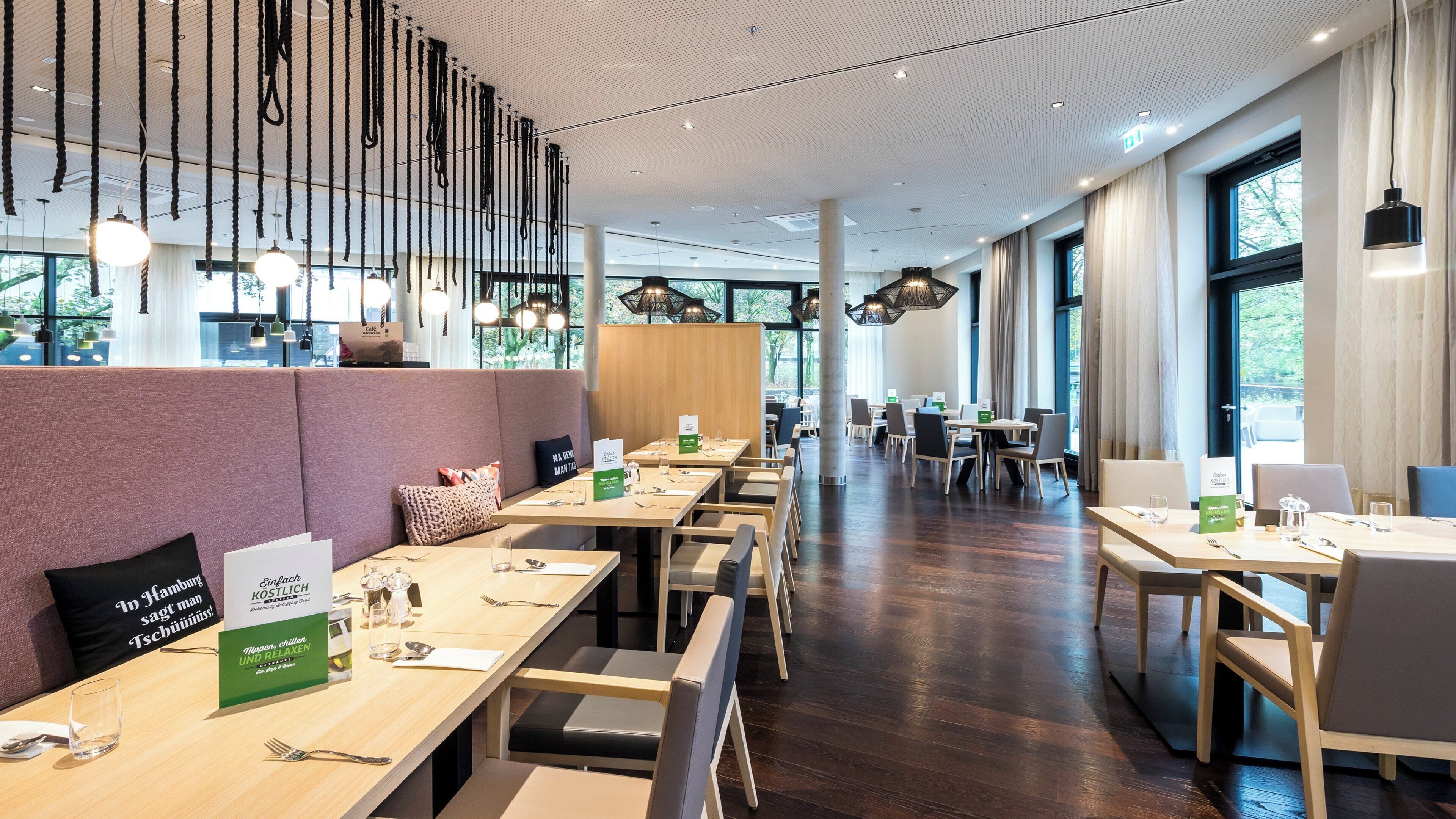 Ein modernes Restaurant mit langen Gemeinschaftstischen, einzelnen Sitzecken und hängenden Pendelleuchten.